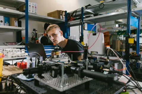 person in industry lab setting surrounded by shelfes, boxes, cables, etc.